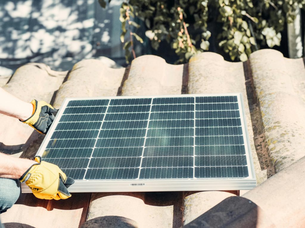 A man placing a solar panel on the roof of a house.